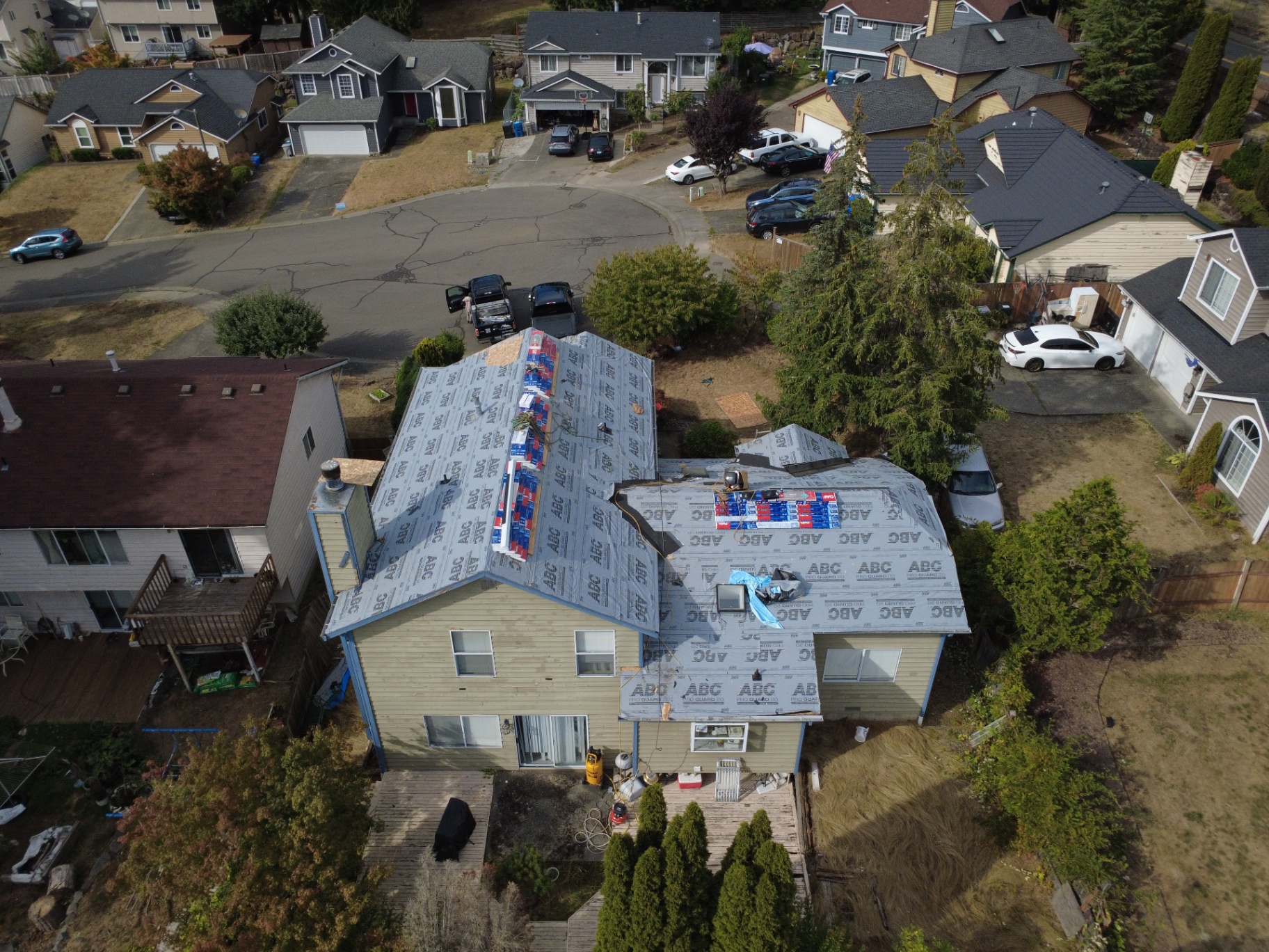 Aerial view of a Western Washington home during emergency roof work, with synthetic underlayment installed and shingle bundles staged on the roof