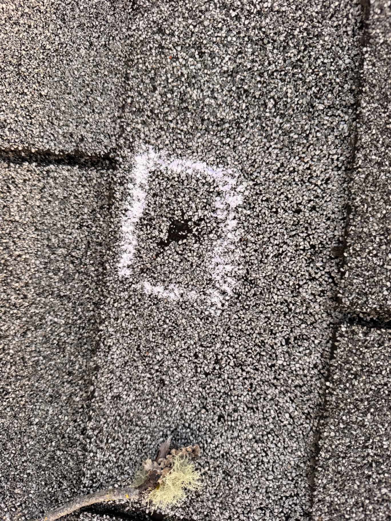 Close-up inspection of a marked puncture in an asphalt roof shingle