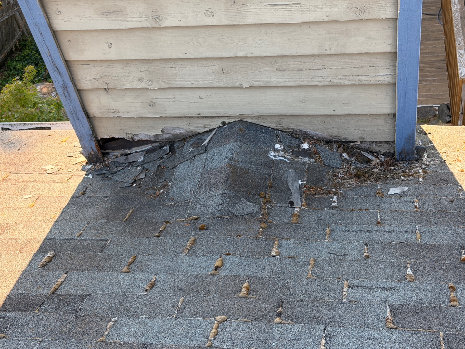 Damaged shingles and deteriorated flashing at a roof-to-wall leak area
