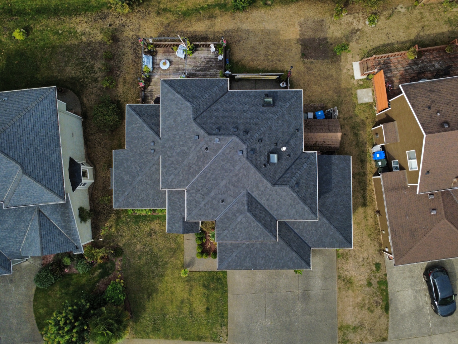 Overhead drone view looking straight down at a completed dark charcoal shingle roof with vents, chimney, and skylight on a home in Covington, Washington